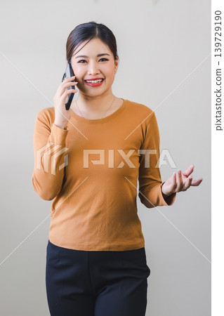 Confident asian woman with friendly smile stands with hand holding smartphone isolated on white background. Confident asian woman with friendly smile stands with hand holding smartphone isolated on white background. 139729190