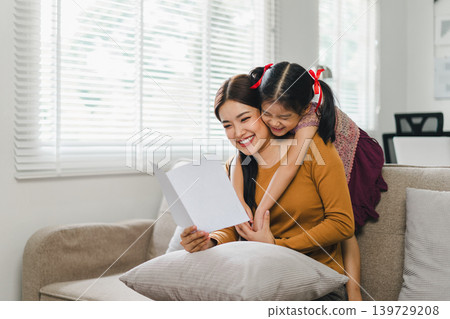 Happy mother's day. Mother receiving a handmade card from her daughter in living room at home. 139729208
