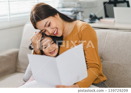 Happy mother's day. Mother receiving a handmade card from her daughter in living room at home. 139729209
