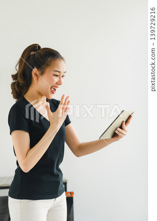 Confident asian woman with friendly smile stands with hand holding digital tablet isolated on white background. Confident asian woman with friendly smile stands with hand holding digital tablet isolated on white background. 139729216
