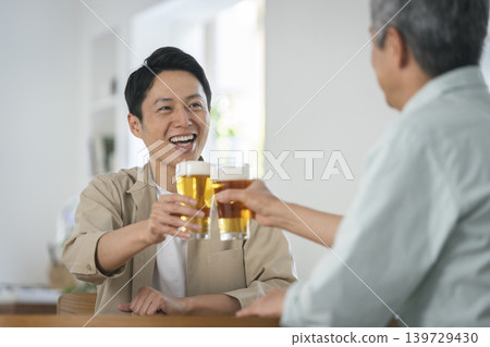 Two men facing each other and toasting with beer. 139729430