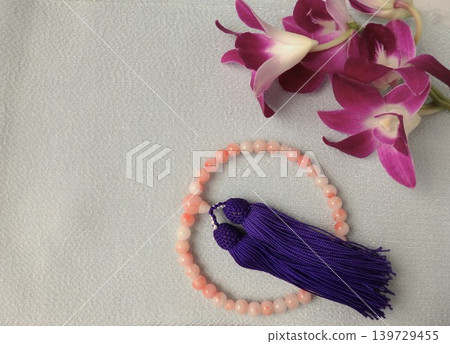 Image of a Buddha statue with pink prayer beads and purple dendrobium orchids. 139729455