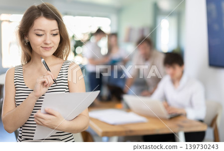 Young woman standing in office with paper documents Young woman standing in office with paper documents 139730243