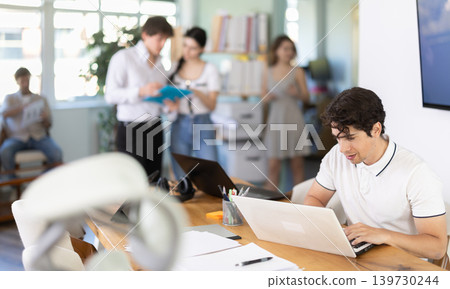 Guy sitting at desk is working on laptop computer. Guy sitting at desk is working on laptop computer. 139730244