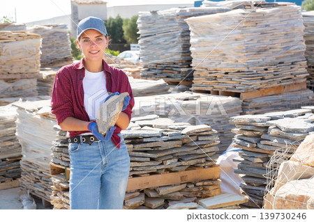 Female builder is choosing natural facing stone in the building store at an open-air construction site Female builder is choosing natural facing stone in the building store at an open-air construction site 139730246