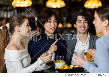 Young friends meeting at table in bar, discussion and drinking beer Young friends meeting at table in bar, discussion and drinking beer 139730247