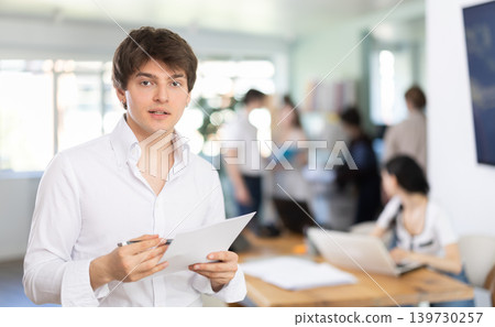 Young man standing in office with paper documents 139730257