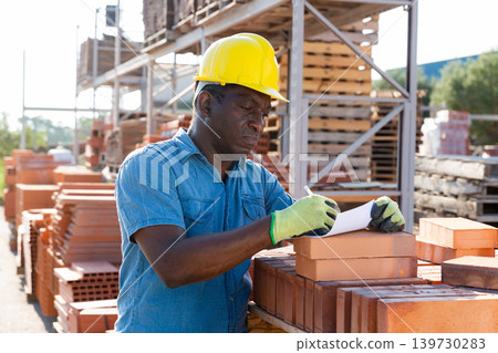 Man filling documentation beside brick stack 139730283