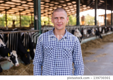 Male farmer posing in cowshed at the cow farm Male farmer posing in cowshed at the cow farm 139730301
