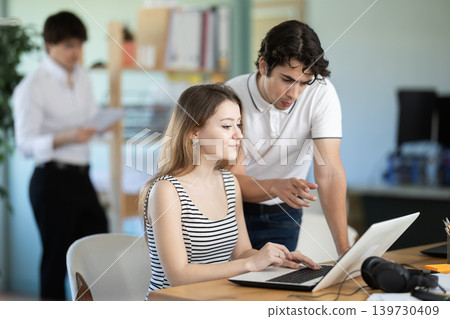 Young man helping young female colleague work on laptop Young man helping young female colleague work on laptop 139730409
