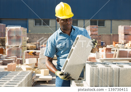 Man holding hollow concrete brick in hands in outdoor warehouse Man holding hollow concrete brick in hands in outdoor warehouse 139730411