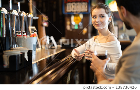 Young woman drinking beer and chatting with man at bar Young woman drinking beer and chatting with man at bar 139730420