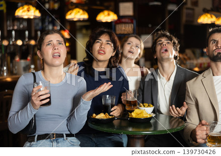 Group of young sports fans upset and worrying during game match on TV in beer pub Group of young sports fans upset and worrying during game match on TV in beer pub 139730426