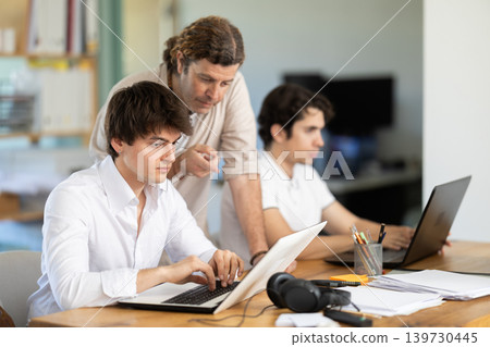 Several employees sit at desk during working day, working with laptop and paper documents. Several employees sit at desk during working day, working with laptop and paper documents. 139730445