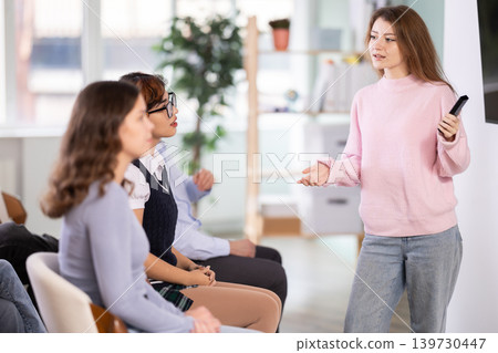 Female lecturer communicates with students, controls projector using remote control. Female lecturer communicates with students, controls projector using remote control. 139730447