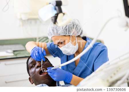 Female dentist performing teeth treatment to adult man at clinic Female dentist performing teeth treatment to adult man at clinic 139730606