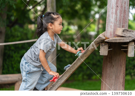 preschool child girl practicing climbing on wooden bouldering wall at outdoor playground preschool child girl practicing climbing on wooden bouldering wall at outdoor playground 139730610