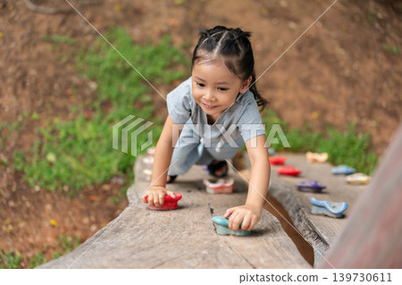 preschool child girl practicing climbing on wooden bouldering wall at outdoor playground 139730611