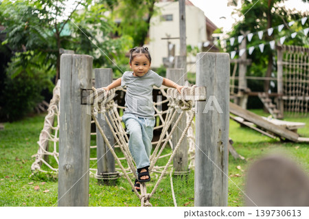 preschool child girl playing and walking on wooden rope bridge at outdoor playground in park preschool child girl playing and walking on wooden rope bridge at outdoor playground in park 139730613