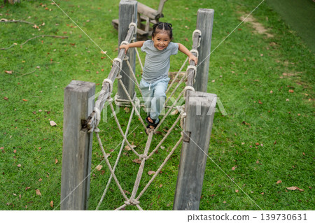 preschool child girl playing and walking on wooden rope bridge at outdoor playground in park preschool child girl playing and walking on wooden rope bridge at outdoor playground in park 139730631