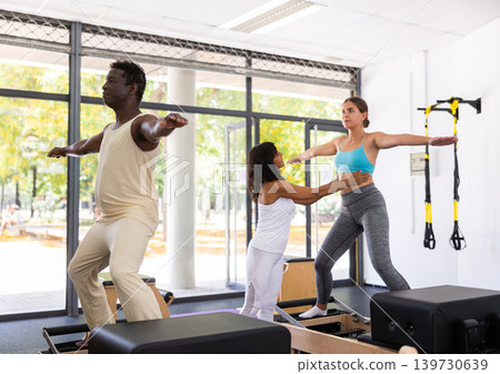 Man and woman doing exercises in pilates gym with man instructor 139730639