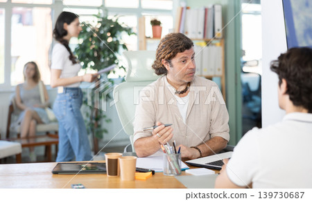 Man bank employee sits at desk and communicates with unrecognizable male client. Man bank employee sits at desk and communicates with unrecognizable male client. 139730687