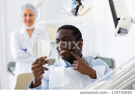 Man looking in mirror to evaluate results of dental restoration procedure Man looking in mirror to evaluate results of dental restoration procedure 139730698