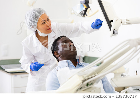 Man patient and woman dentist looking at monitor during consultation Man patient and woman dentist looking at monitor during consultation 139730717