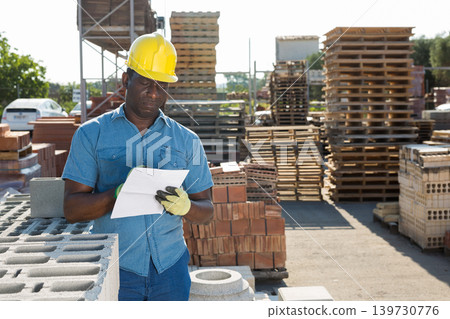 Worker filling documentation beside hollow block stack outdoors Worker filling documentation beside hollow block stack outdoors 139730776