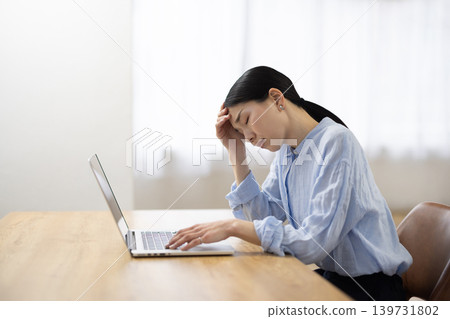 A Japanese woman with a negative expression sits at her desk in front of her computer. A Japanese woman with a negative expression sits at her desk in front of her computer. 139731802