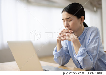 A Japanese woman with a negative expression sits at her desk in front of her computer. A Japanese woman with a negative expression sits at her desk in front of her computer. 139731803