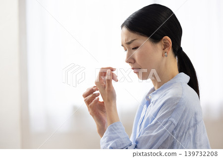 A Japanese woman scratching her hand with a pained expression. A Japanese woman scratching her hand with a pained expression. 139732208