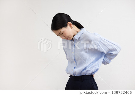 A Japanese woman stands in front of a white wall, hands on her hips, with a pained expression on her face. A Japanese woman stands in front of a white wall, hands on her hips, with a pained expression on her face. 139732466