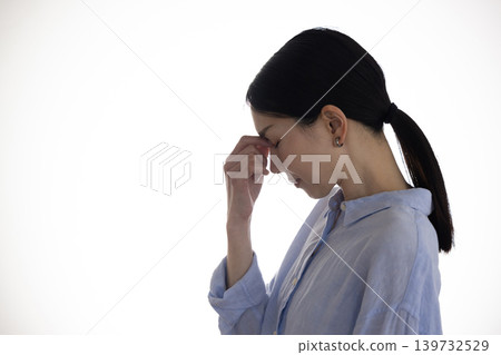 A middle-aged woman with her hand on her temple stands in front of a white background. A middle-aged woman with her hand on her temple stands in front of a white background. 139732529