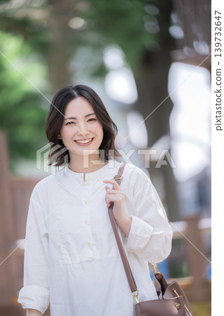 一位微笑的女子漫步在綠樹成蔭的小鎮中,展現出自然的生活方式;非常適合通勤或休閒郊遊,她直視鏡頭。 一位微笑的女子漫步在綠樹成蔭的小鎮中,展現出自然的生活方式;非常適合通勤或休閒郊遊,她直視鏡頭。 139732647