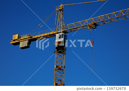 Yellow tower crane against clear blue sky at construction site 139732678