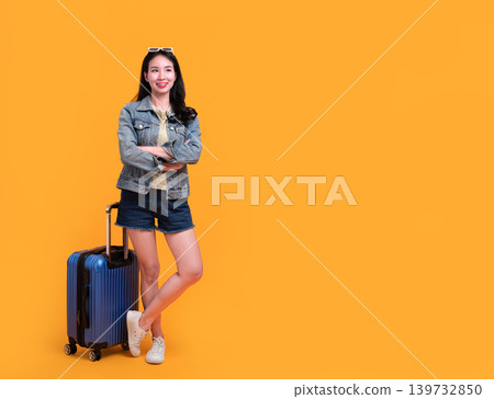 Happy Asian woman traveler standing and holding suitcase isolated on yellow background, Tourist girl having cheerful holiday trip concept, Full body composition. 139732850