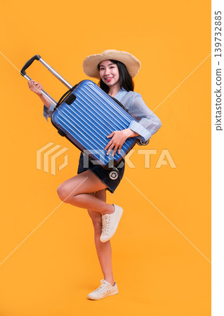 Happy Asian woman traveler standing and holding suitcase isolated on yellow background, Tourist girl having cheerful holiday trip concept, Full body composition. 139732885