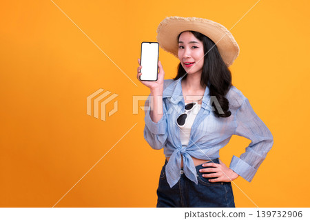 Happy Asian woman woman tourist holding a blank phone isolated on yellow background. Happy Asian woman woman tourist holding a blank phone isolated on yellow background. 139732906