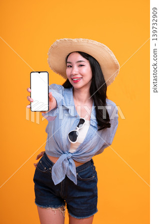 Happy Asian woman woman tourist holding a blank phone isolated on yellow background. Happy Asian woman woman tourist holding a blank phone isolated on yellow background. 139732909