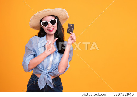 Happy Asian woman woman tourist showing credit card isolated on orange background. Happy Asian woman woman tourist showing credit card isolated on orange background. 139732949