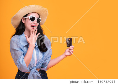 Happy Asian woman woman tourist showing credit card isolated on orange background. Happy Asian woman woman tourist showing credit card isolated on orange background. 139732951