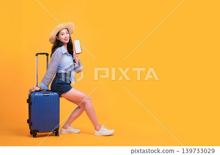 Happy Asian woman traveler standing and holding suitcase isolated on yellow background, Tourist girl having cheerful holiday trip concept, Full body composition. Happy Asian woman traveler standing and holding suitcase isolated on yellow background, Tourist girl having cheerful holiday trip concept, Full body composition. 139733029