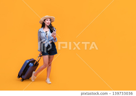 Happy Asian woman traveler standing and holding suitcase isolated on yellow background, Tourist girl having cheerful holiday trip concept, Full body composition. Happy Asian woman traveler standing and holding suitcase isolated on yellow background, Tourist girl having cheerful holiday trip concept, Full body composition. 139733036