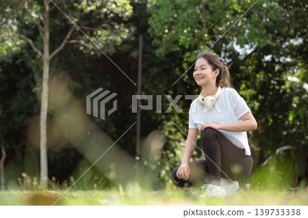 Young Asian woman doing stretches before exercising or training in a park before training, enjoying a healthy lifestyle. Young Asian woman doing stretches before exercising or training in a park before training, enjoying a healthy lifestyle. 139733338