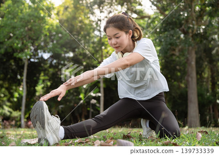 Young Asian woman doing stretches before exercising or training in a park before training, enjoying a healthy lifestyle. Young Asian woman doing stretches before exercising or training in a park before training, enjoying a healthy lifestyle. 139733339