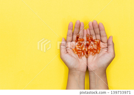 Close up of a person's hand holding several golden softgel capsules. Concept of taking daily dose of vitamin or fish oil supplement for healthcare and wellness. Close up of a person's hand holding several golden softgel capsules. Concept of taking daily dose of vitamin or fish oil supplement for healthcare and wellness. 139733971
