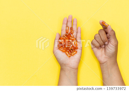 Close up of a person's hand holding several golden softgel capsules. Concept of taking daily dose of vitamin or fish oil supplement for healthcare and wellness. Close up of a person's hand holding several golden softgel capsules. Concept of taking daily dose of vitamin or fish oil supplement for healthcare and wellness. 139733972