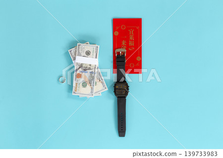 Chinese New Year prosperity concept with US dollar bills, Silver Ring, Wristwatch and a red envelope (angpao) with Chinese text that translates to "Good fortune comes" on blue background. 139733983