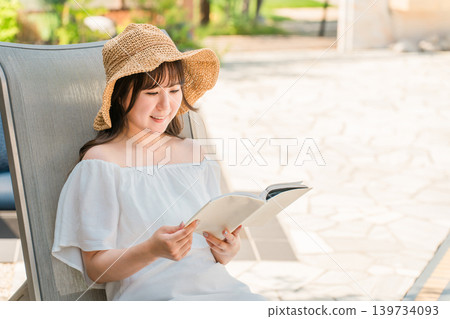 Young Asian woman reading a book while sitting on a recliner by the pool Young Asian woman reading a book while sitting on a recliner by the pool 139734093